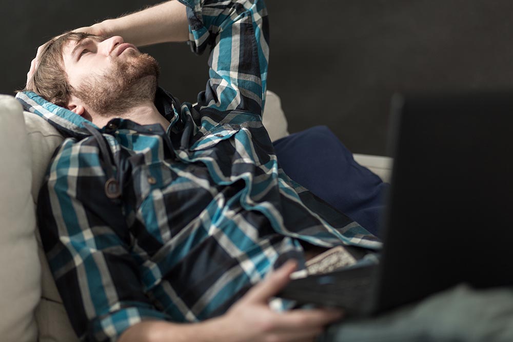 Depressed man sitting on the couch with laptop - Contra Costa divorce attorneys at Ryan Family Law